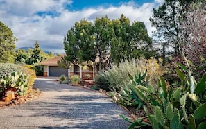 Un camino de entrada residencial que lleva a una casa con garaje, rodeada de diversos cactus y plantas del desierto.