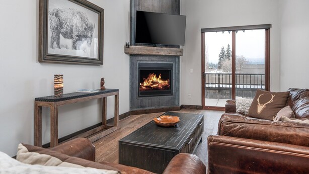 A living room with a fireplace, a mounted TV, and a large window. - New! Downtown Whitefish with private hot tub and balcony (Whitefish)