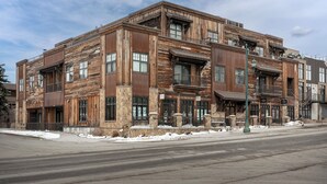 A multi-story building with a rustic wooden facade, large windows, and a stone base. - New! Downtown Whitefish with private hot tub and balcony (Whitefish)