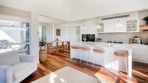 Una cucina moderna con mobili bianchi, un'isola centrale con sgabelli da bar e un'area pranzo con tavolo e sedie in legno.