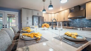 Une cuisine moderne avec des plans de travail en marbre, un îlot central agrémenté de serviettes jaunes et des luminaires suspendus.