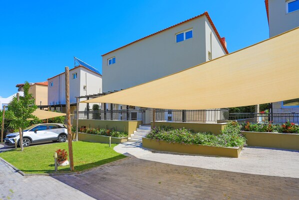 A residential building with a paved courtyard, a car parked outside, and a large sunshade over the seating area. - Your private haven in breathtaking Halkidiki (Hanioti)