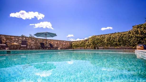 A clear swimming pool with lounge chairs and an umbrella, surrounded by a stone wall and greenery. - Your Luxury Escape in Corfu’s Tranquil Countryside (Akrokefalo Gouvia)
