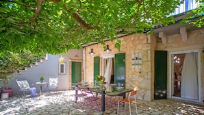 A stone-floored patio with a table and chairs, a potted plant, and a staircase leading to an upper level. - Your Luxury Escape in Corfu’s Tranquil Countryside (Akrokefalo Gouvia)