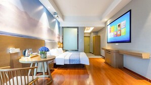 A modern hotel room with a bed, a desk with a chair, a TV, and a small table with a vase of flowers.