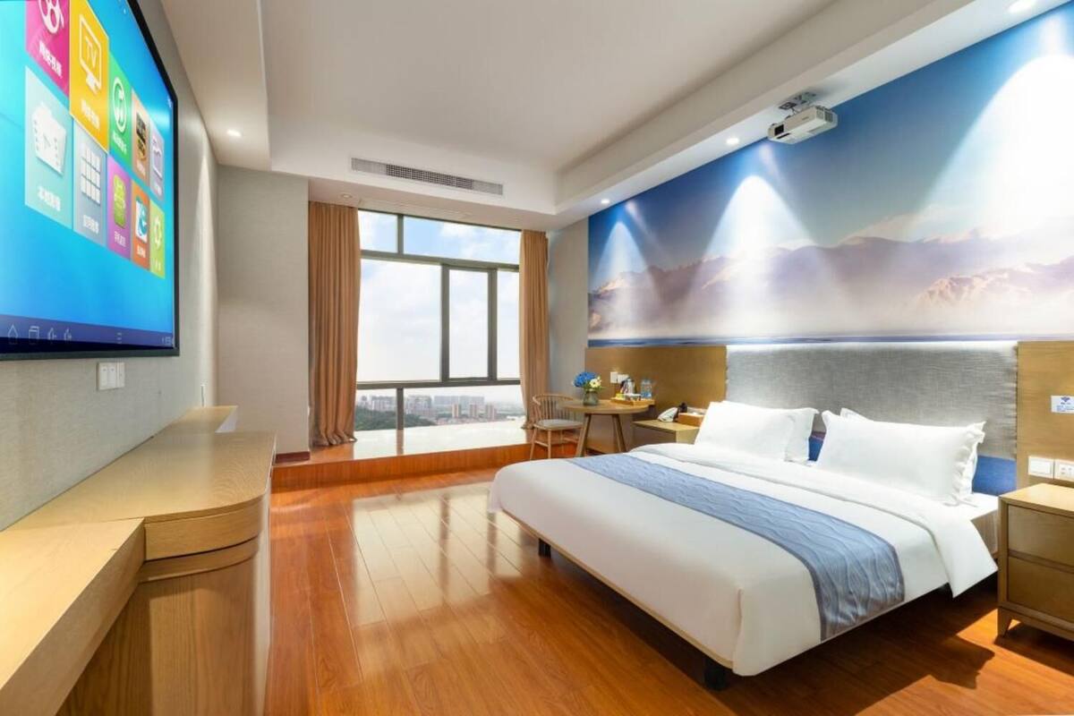 Een hotelkamer met een groot bed, een bureau, een stoel, een kleine tafel en een groot raam met uitzicht op de stad.