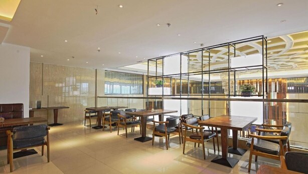 A modern restaurant with wooden tables and chairs, large windows, and a high ceiling with recessed lighting.