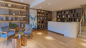 A modern lobby with a reception desk, wooden flooring, and a staircase.