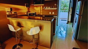 Uma cozinha com ilha central, dois banquetas altas, micro-ondas e geladeira.