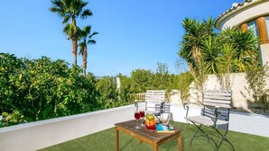 An outdoor seating area with a wooden table and chairs, surrounded by lush greenery and palm trees. - Villa Kmar by Villa Plus (El Poble Nou de Benitatxell)