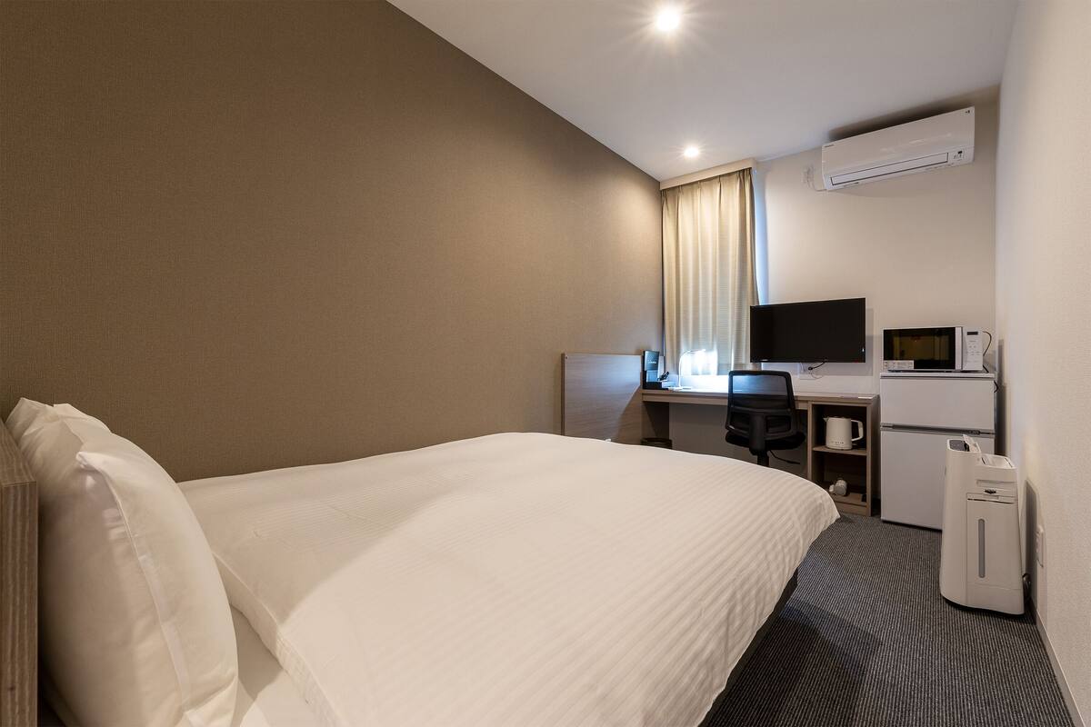A hotel room with a bed, a desk with a computer, a television, and a microwave.