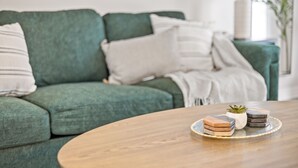 Un sofà verd amb coixins blancs i estrisats, una petita planta en test i un safata amb sabates al damunt d'una taula de fusta.