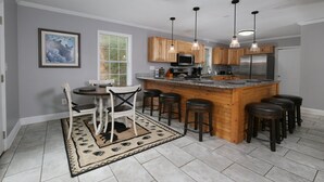 A kitchen with a central island, wooden cabinets, bar stools, a dining table with chairs, pendant lights, and a framed picture on the wall. - Hot Tub Soaks Under the Stars, Firepit S'mores & Secluded Mountain Vibes - A Country Retreat (Gatlinburg)