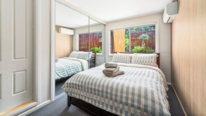 Een slaapkamer met twee bedden, een grote spiegel en een raam met uitzicht op een houten schutting en begroeiing.