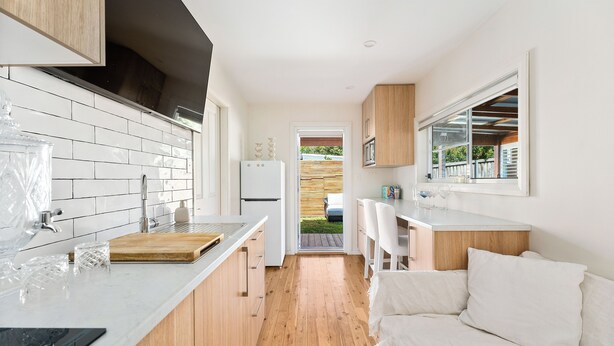 Een moderne keuken met witte tegels, houten kastjes, een houten vloer en een witte bank.