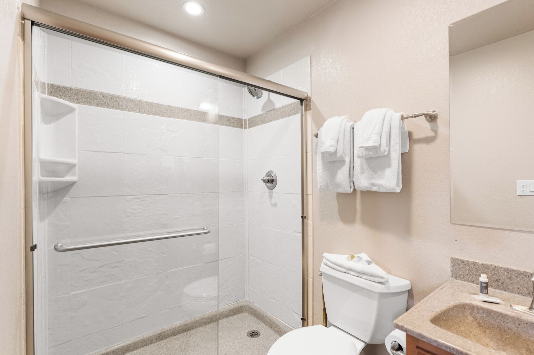 A modern bathroom with a glass-enclosed shower, a toilet, and a sink with a granite countertop.