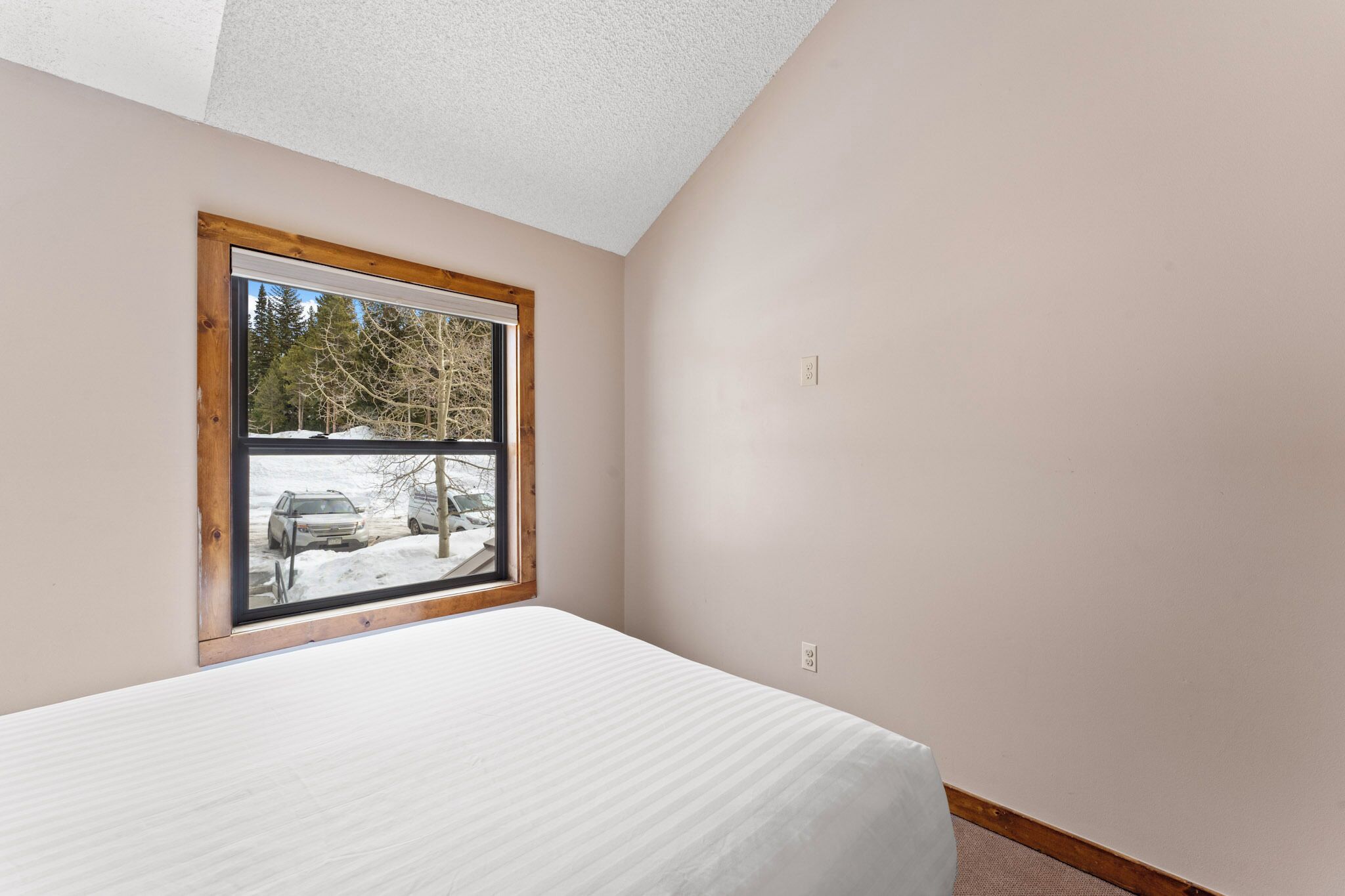 A bedroom with a large window, a bed, and a view of a snowy parking lot.