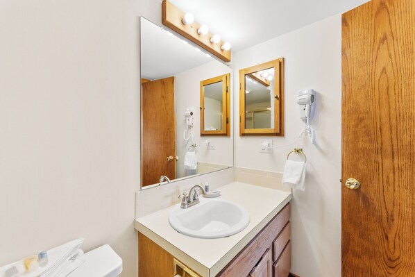 Une salle de bain avec un lavabo blanc, deux miroirs, un sèche-cheveux et un porte-serviettes.