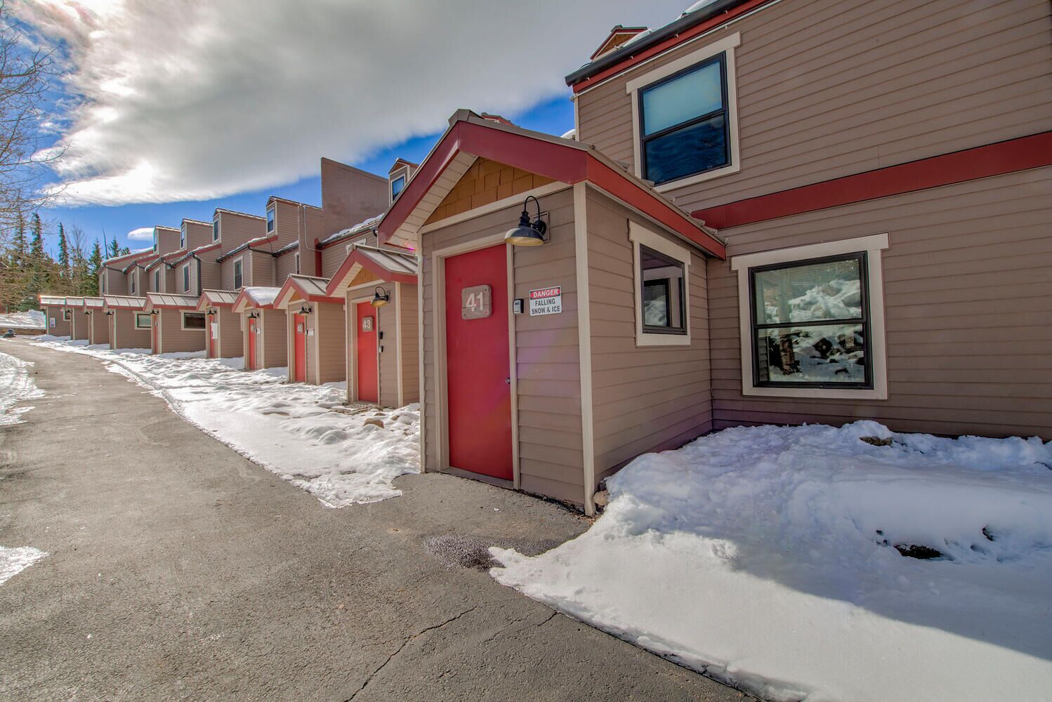 A row of single-story cabins with red doors, numbered 41 and 42, in a snowy setting.