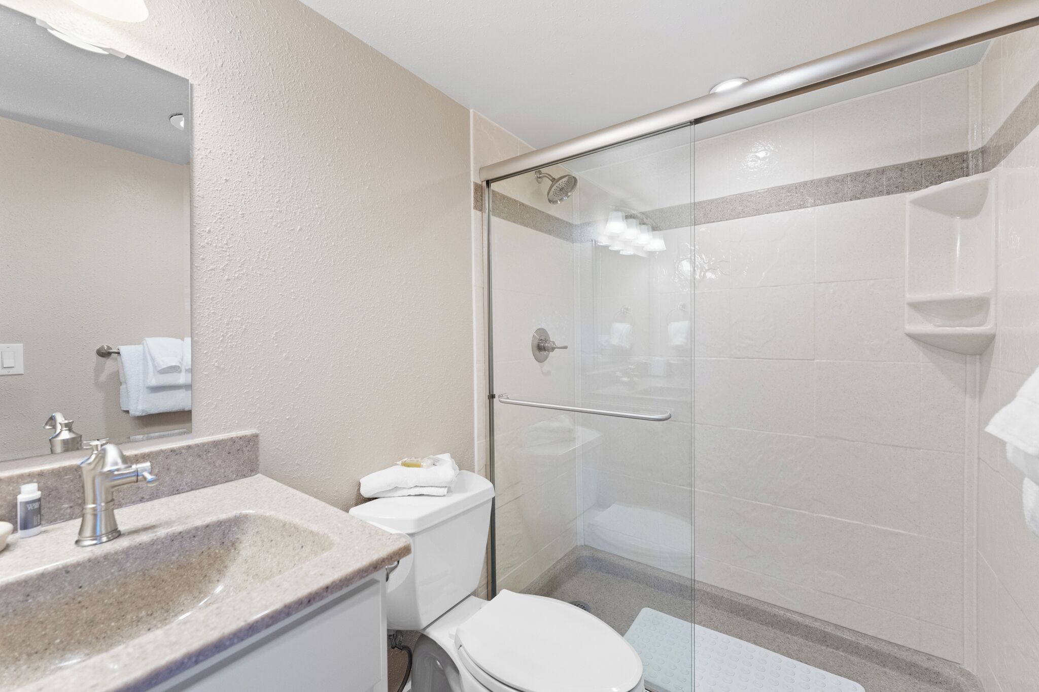A modern bathroom with a glass-enclosed shower, a sink with a marble countertop, and a toilet.