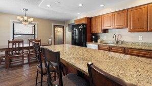 Eine Küche mit Granit Arbeitsplatten, Holzschränken, einem schwarzen Kühlschrank und einer Chandelier.