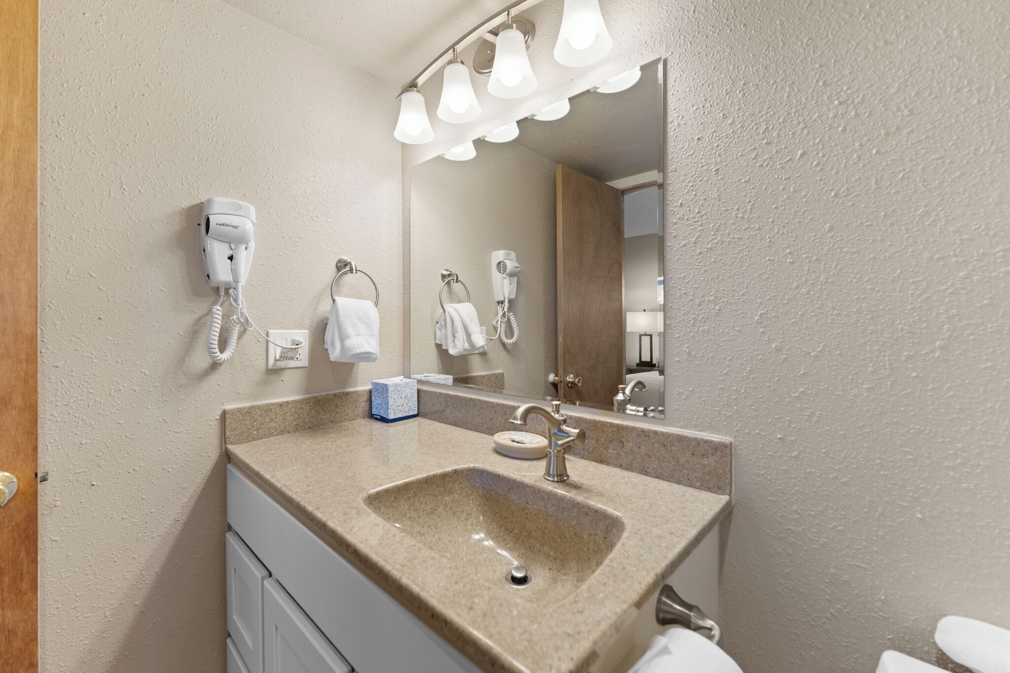 Un baño con un lavabo color beige, un espejo y dos secadores de pelo montados en la pared.
