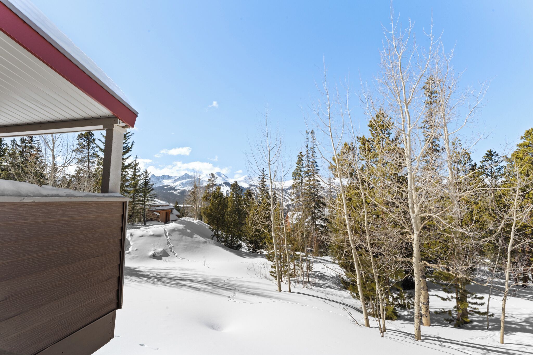 A wooden cabin with a red roof overlooking a snowy landscape with trees and mountains in the background.