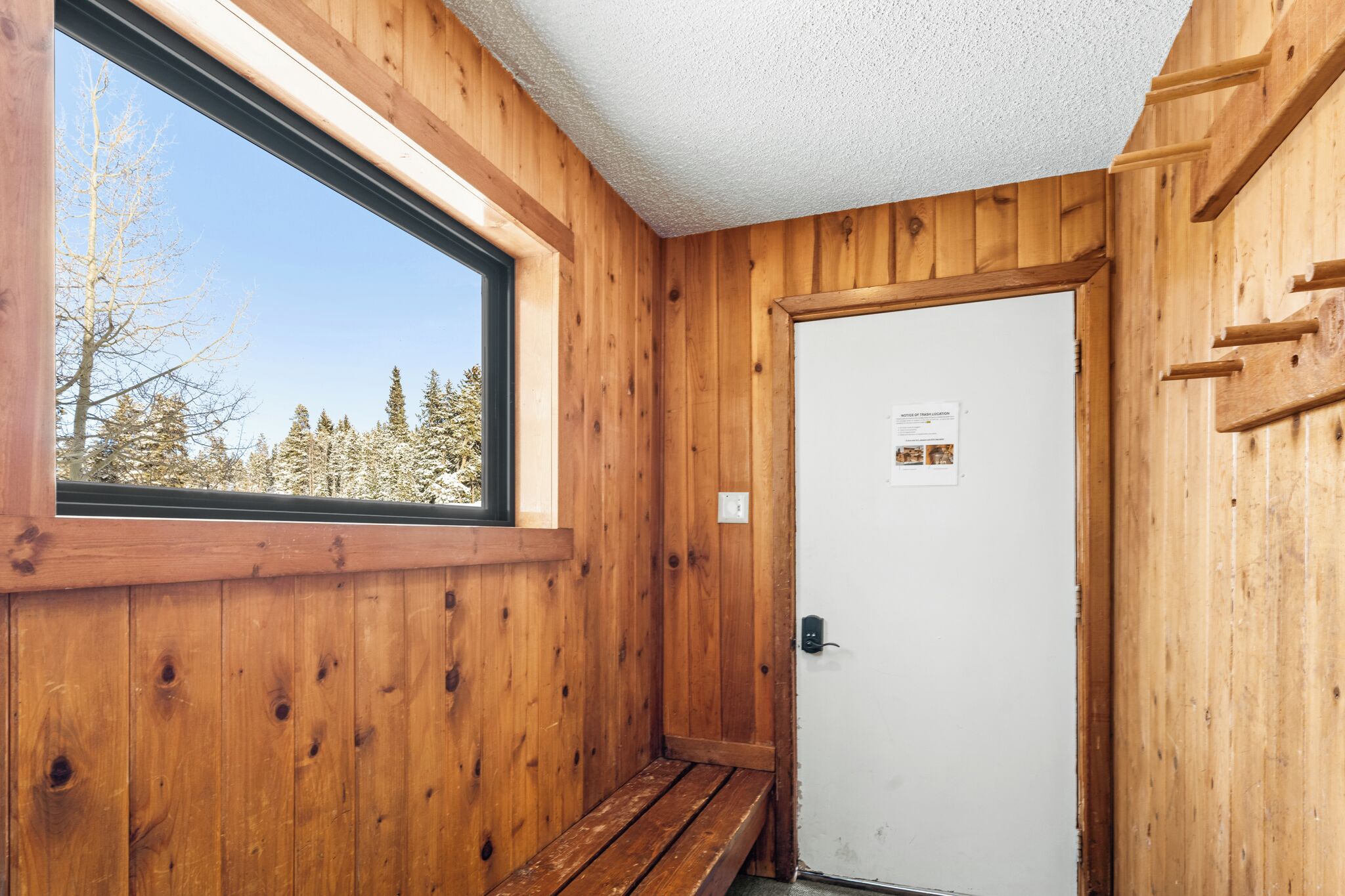 Ein Holzblockhaus-Innenraum mit großem Fenster, einer Tür und einer Bank.