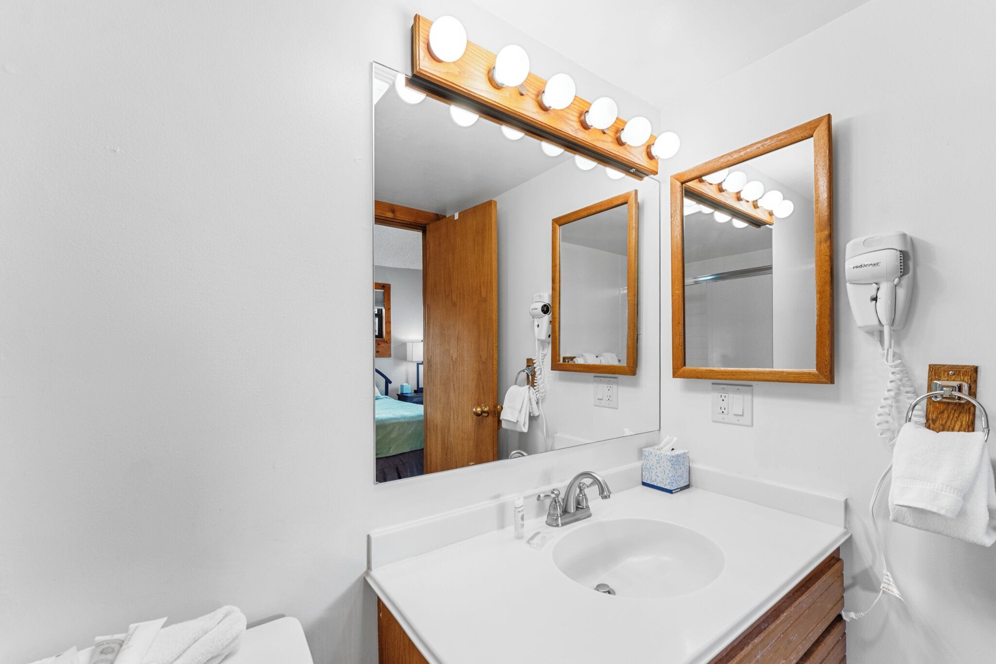 Une salle de bain dotée d’un grand miroir, d’un meuble-lavabo et d’un sèche-cheveux fixé au mur.