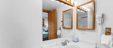 Une salle de bain dotée d’un grand miroir, d’un meuble-lavabo et d’un sèche-cheveux fixé au mur.