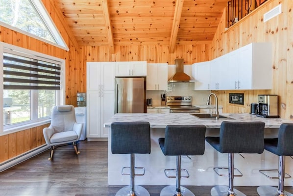 A modern kitchen with wooden walls, a large island with bar stools, and a stainless steel refrigerator.