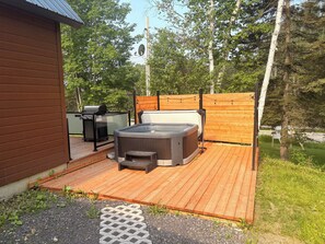 Eine Holzterrasse mit Whirlpool, Grill und einem kleinen Tisch.