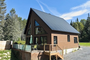 A modern two-story cabin with a sloped roof, large windows, and a deck with outdoor furniture.
