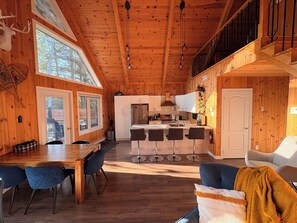 A wooden cabin interior with a dining area, kitchen, and a balcony.