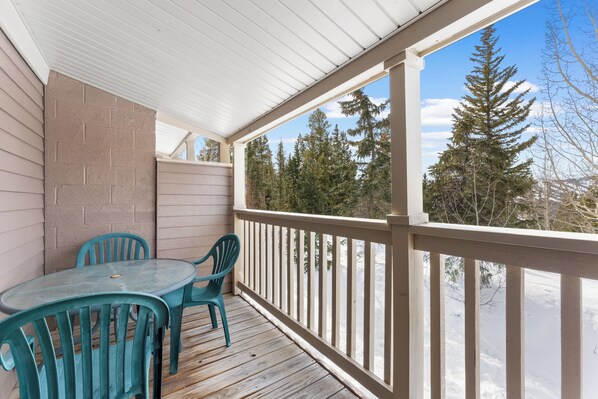 A covered porch with a table and chairs, a view of trees and snow. - Rr47b3 (Breckenridge)