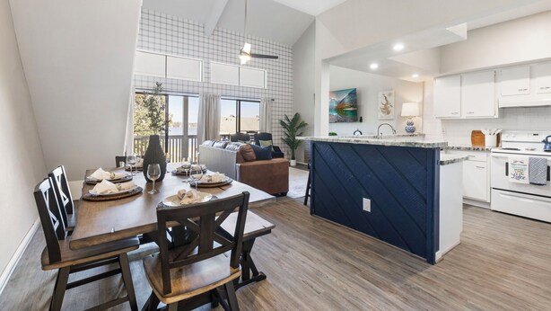 A modern kitchen with white cabinets, a central island, and a dining area with wooden chairs and a table set for four. - Lux Condo on Lake Conroe, Lakeview, Pool, Game room (Montgomery)