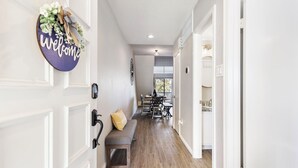 A hallway with a bench, a welcome sign, and a dining area in the background. - Lux Condo on Lake Conroe, Lakeview, Pool, Game room (Montgomery)