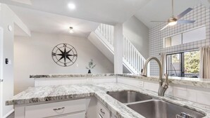 A kitchen with white cabinetry, granite countertops, a stainless steel sink, and a ceiling fan. - Lux Condo on Lake Conroe, Lakeview, Pool, Game room (Montgomery)