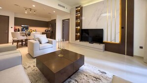 Ein modernes Wohnzimmer mit einem großen Flachbildfernseher, einem Couchtisch und einer Sitzecke inklusive Sofa und Sesseln.
