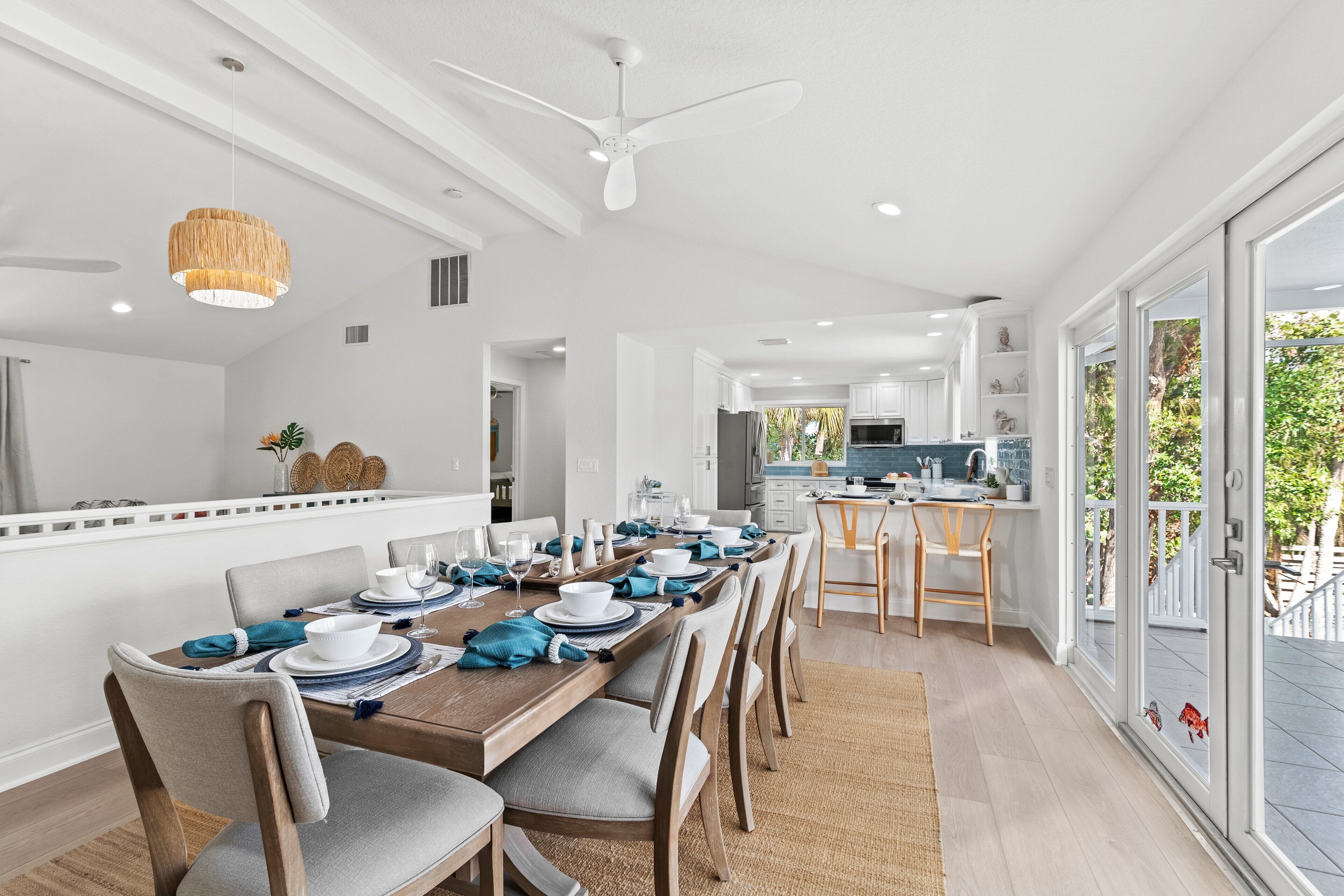 Un espace de salle à manger moderne, avec une longue table en bois pouvant accueillir six personnes, des chaises blanches et un ventilateur de plafond.