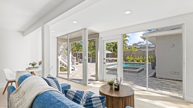 A modern living room with a large sofa, a coffee table, and a view of a swimming pool and outdoor area. - Shore Thing | Luxe Pool Oasis, Hot Tub, Siesta Key Beach (Siesta Key)