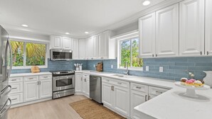 A modern kitchen with white cabinets, stainless steel appliances, and a blue backsplash. - Shore Thing | Luxe Pool Oasis, Hot Tub, Siesta Key Beach (Siesta Key)