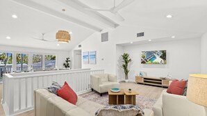 A spacious living area with a white ceiling, ceiling fan, and large windows. There is a white sofa, a small coffee table, and a potted plant. - Shore Thing | Luxe Pool Oasis, Hot Tub, Siesta Key Beach (Siesta Key)