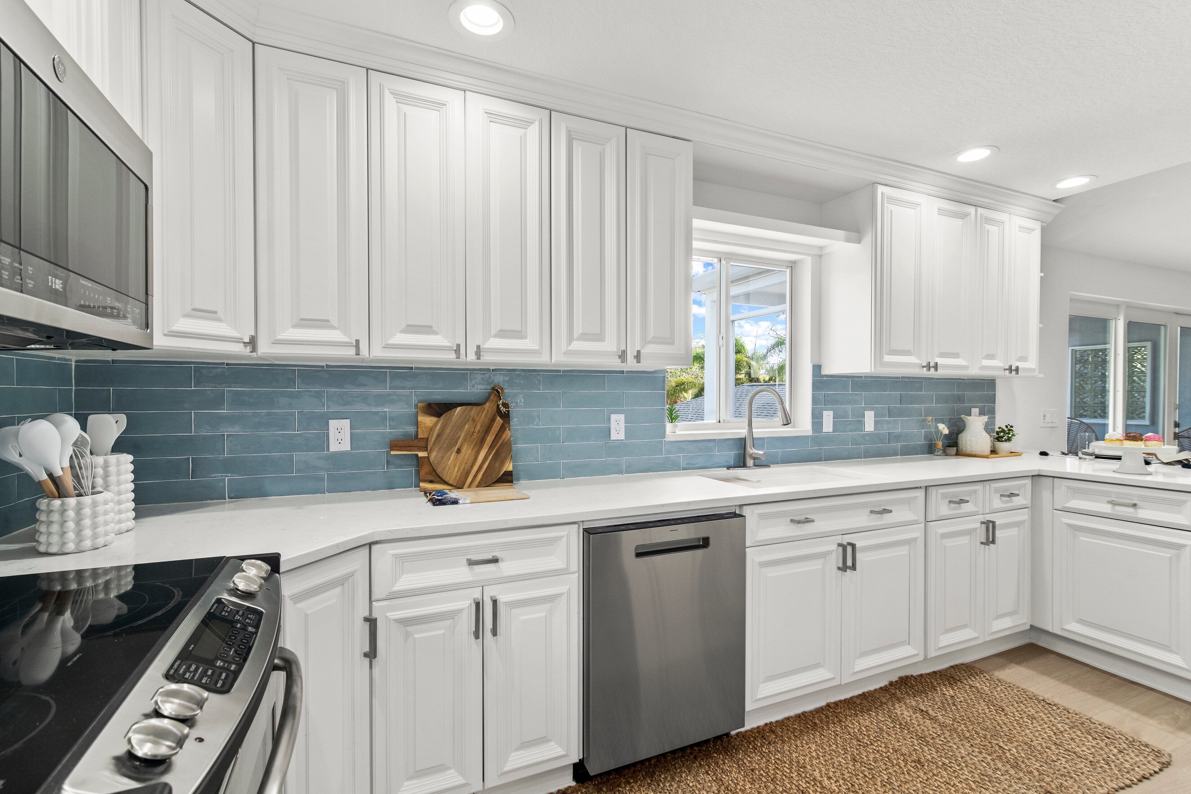 A modern kitchen with white cabinetry, a stainless steel dishwasher, and a blue tiled backsplash.