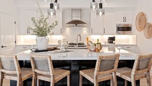 A modern kitchen with white cabinetry, a central island with seating, pendant lighting, and a stainless steel range hood. - Luxe Two Story Condo in the Heart of Downtown SB! (Santa Barbara)