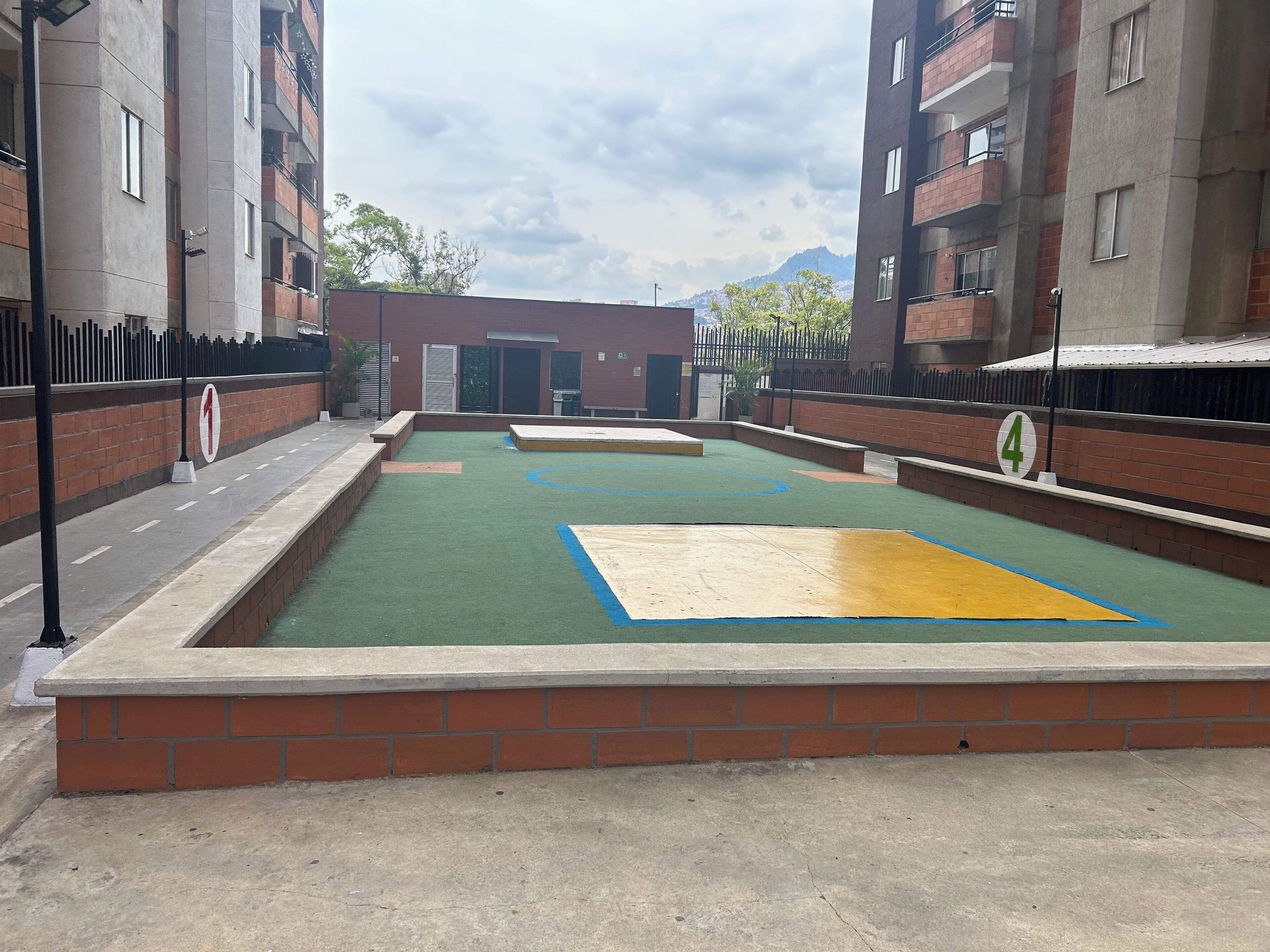 Una cancha de baloncesto al aire libre rodeada de edificios de ladrillo, con cielo despejado y montañas a lo lejos.