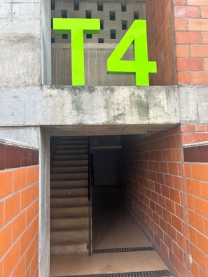 A building entrance with a concrete wall and a brick section. A large green 'T4' sign is visible above the entrance. - Depa Bello Toledo Campestre (Bello)