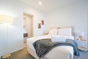 A hotel room with a bed, bedside tables, a lamp, and a door leading to a bathroom. - 2 Bedrooms in Prime Location with Free Parking (Auckland)