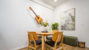En matplats med ett träbord, två stolar, en gitarr, en växt och ett inramat konstverk på väggen.
