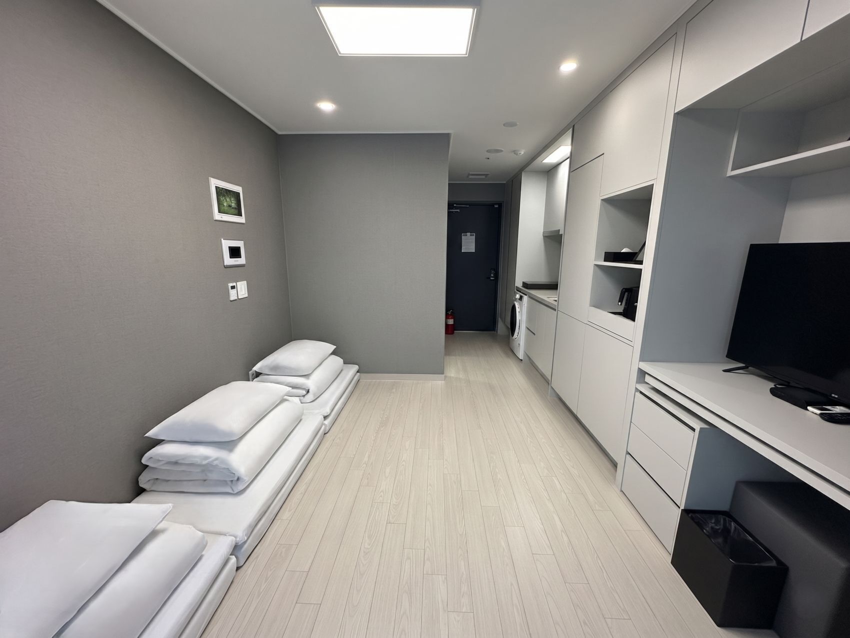 A hotel room with a bed, a TV, a washing machine, and a small kitchenette.